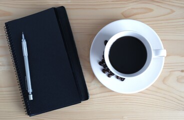 cup of coffee with beans and black notebook for copy space on wooden table background 