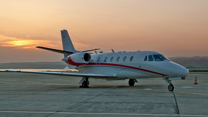 Fototapeta na wymiar Side view of white red midsize business jet with turbofan engines at sunset evening time at the airport. Modern technology in fast transportation, business travel and tourism, aviation concept.