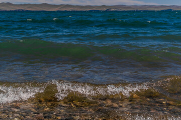 bright blue emerald green waves of lake baikal in the light of the sun in summer, mountains on the horizon, stones in water, coast