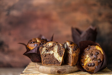 Soft and moist chocolate banana muffins with dark chocolate drops in wooden box, rustic table. Homemade baked twisted cupcakes. Natural light, selective focus, copy space