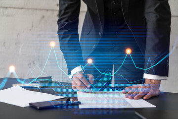 Businessman in suit signs contract. Double exposure with financial chart hologram. Man signing mortgage agreement. Real estate market analysis and investment concept.