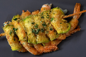 Crayfish skewer with slices of zucchini and breadcrumbs.