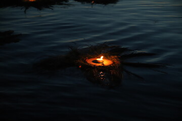 a burning candle in a wreath floats on the water at night