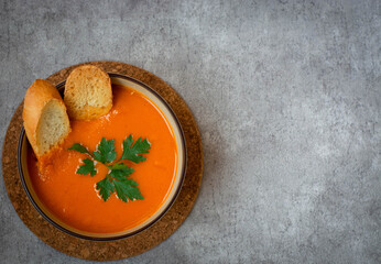 Pumpkin and carrot soup with cream and parsley on a dark concrete background, top view of the space.