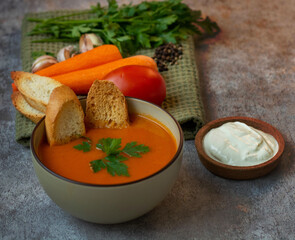 Pumpkin soup in a bowl with crackers, with fresh pumpkins, garlic and parsley, carrots, tomatoes, on a dark background.