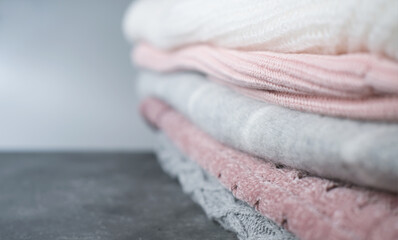 a pile of knitted sweaters in grey and pink colors. winter season clothes. selective focus. textured fabrics background. copy space for text or advertising. shallow depth of field.