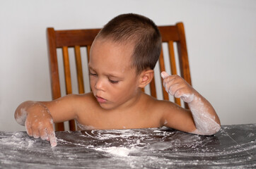 little boy plays with white flour on a black wooden table. in a natural setting in natural light. without editor