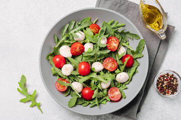 Diet and healthy salad with arugula, cherry tomatoes, mozzarella cheese and olive oil on white background