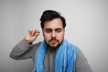 Bearded man cleaning his ears with blue towel, sitting over white wall. Space for text.