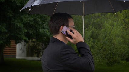 Сlose up of a businessman holding an umbrella over his head while talking on a mobile phone.