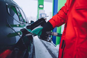 Cropped image of male hand holding gas station pistol for refill for automobile in winter, gas...