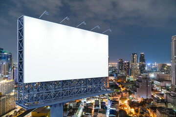 Blank white road billboard with Bangkok cityscape background at night time. Street advertising poster, mock up, 3D rendering. Side view. The concept of marketing communication to sell idea.