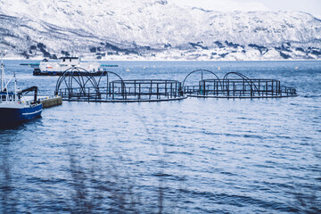 Industrial construction on salmon farm in freezing scandinavian lake water near high mountains in snow, scenic nature of scandinavian and fishing place in sea