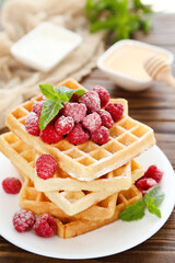 Tasty waffles with fresh raspberries and mint leafs on brown wooden background