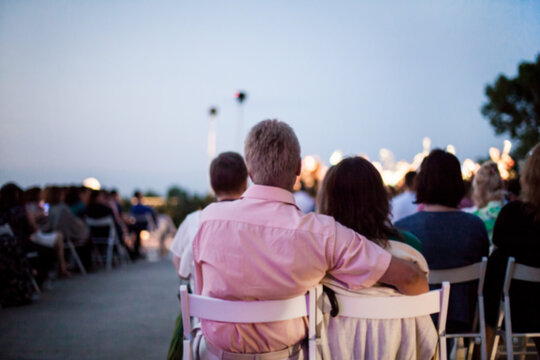 People Are Watching A Concert Of Classical Music. Blurred Young And Adult Women And Men And Other People Watching Listening To Concert Of Classical Band In Daylight Outdoor Enviroment.