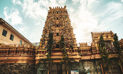 Hindu temple full of colorful ornaments against a blue sky on a sunny day.
