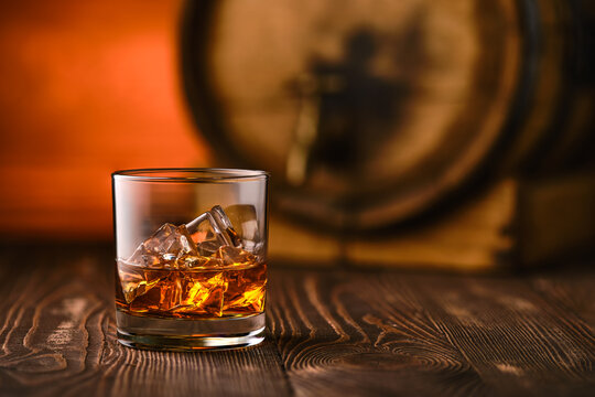 Glass of whiskey with ice with barrel on background