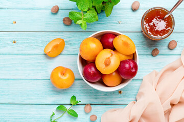 Yellow and red plums in a plate and jar of plum jam on blue wooden table flat lay, autumn fruit preserves concept, copy space