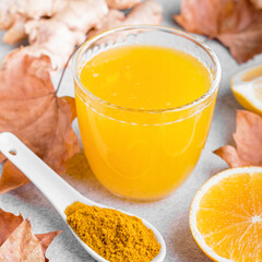 Immune boosting drink with citrus fruits, ginger, turmeric. Drink or smoothie with yellow fall leaves for autumn or virus season on neutral beige background