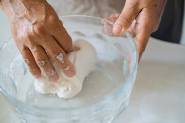 An old man's hand, an Asian woman kneading the ingredients to make bread dough.
