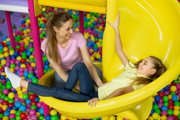 Fototapeta na wymiar Mother and her daughter having good time on slide at kids playground, indoors