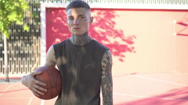 Young man with tattoos on the background of a basketball court. Modern youth image