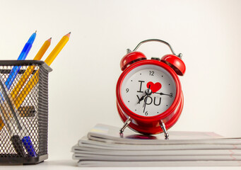 A red alarm clock stands on a stack of school exercise books. Back white background.