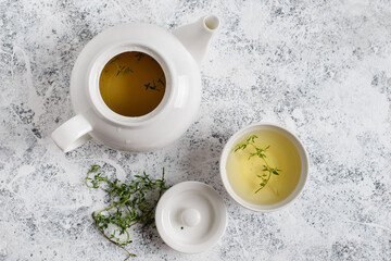 Herbal tea in white teapot and white boul and thyme stalks on light textured background, top view