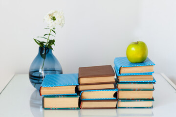 Cozy home interior decor: stack of books, green apple and vase with white flower on a glass table. Distance home education.Quarantine concept of stay home.