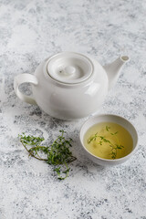 Obraz na płótnie Canvas Herbal tea in white teapot and white boul and thyme stalks on light textured background