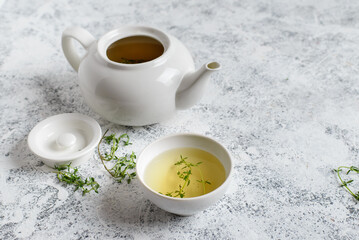 Obraz na płótnie Canvas Herbal tea in white teapot and white boul and thyme stalks on light textured background