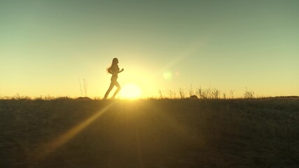 running after sun. training jogging. healthy beautiful girl is engaged in fitness, jogging in country in sun. Jogger girl breathes fresh air on field. Free young woman runs in summer park at sunset.