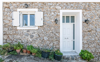 Fototapeta na wymiar white door and window frames on traditional house stone wall facade with flowerpots