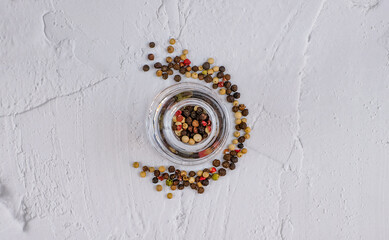 Mix colored pepper corns in glass bottle on white textured background, top view with copy space