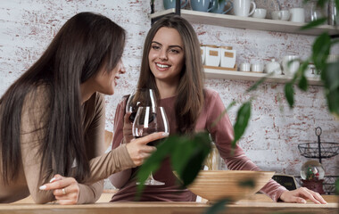 Two pretty girls having a glass of red wine at the kitchen
