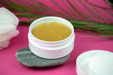 golden under eyes patches in a white container, anti aging skin care, female body care background, pink backdrop