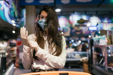 Fototapeta na wymiar Woman with the surgical mask and the gloves is shopping in the supermarket