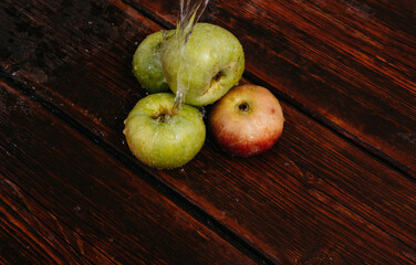 Splashes of clean water pour over freshly picked apples of the autumn harvest. Red and green apples lie on the mahogany wooden kitchen table, and water drips from the top.