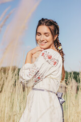Portrait happy beautiful girl with braided hair relax and have fun on wheat countryside field. Cheerful young attractive woman in long embroidery traditional dress enjoy summer nature on farmland