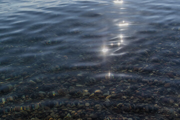 sun glare and colorful  pebbles in the clear morning water of lake baikal, ripples, coast, summer