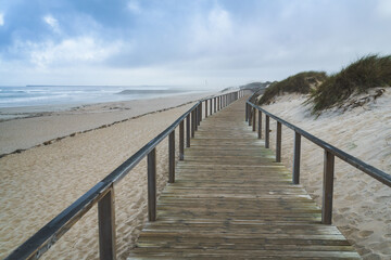 a wooden walkway in the sand of the ocean coast; cloudy skies and fog in the distance