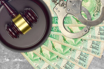 1 Brazilian real bills and judge hammer with police handcuffs on court desk. Concept of judicial...