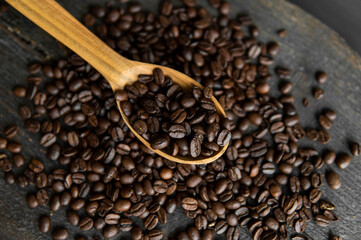 Fresh roasted arabica coffee beans in a wooden spoon and scattered coffee beans on a wooden table.