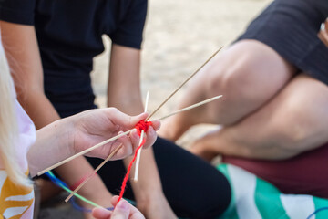 Hand weaving mandalas. A teacher on the beach shows her students how to weave decorative patterns. Creation of special symbols. Training and manual labor concept.