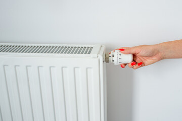 Woman Hand with Red nail laquer Adjusting The Knob Of Heating Radiator. The valve from the radiator - Heating. Hand adjusting thermostat valve of heating radiator in a room on white background.