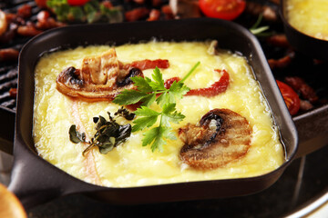 Delicious traditional Swiss melted raclette cheese served in individual skillets with salami and bacon
