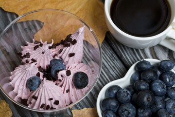 Zephyr in a glass. With biscuit and blueberries. Next to it is a cup of coffee and a saucer of blueberries. Among the maple leaves. On pine boards painted black and white.