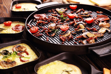 Delicious traditional Swiss melted raclette cheese served in individual skillets with salami and bacon