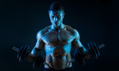 Fototapeta na wymiar Muscular model sports young man with dumbbells in hand on dark background. Fashion portrait of strong brutal guy. Sexy torso. Male flexing his muscles.