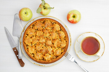Fresh baked homemade apple and cinnamon pie and cup of tea on white wooden table. Top view.